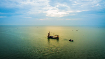 Small towing tugboat dragging the huge Dredger ship in the sea. Drilling industry in the ocean. image for background, wallpaper, advertisement,objects and copy space.
