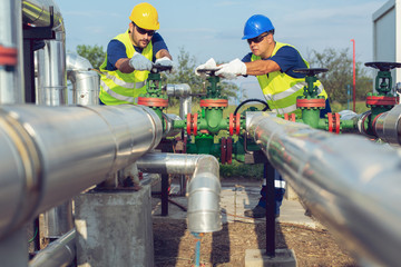 Two petrochemical workers inspecting pressure valves on a fuel tank