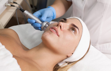Fototapeta premium Beautiful woman getting radio frequency lifting on her face. Professional beautician doing anti-wrinkle facial treatment. Concept of skin care and correction of skin texture.