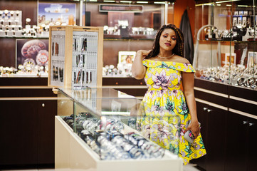 Cute small height african american girl with dreadlocks, wear at coloured yellow dress, on watches store at shopping center.