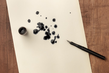 An overhead photo of an ink well with drops of ink and a nib pen, with copy space, on a dark rustic...