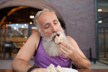 Senior Man eating in georgian restaurant national snack Khinkali, that is a relative to dumplings and raviolli