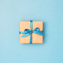 Gift box wrapped in kraft paper tied with blue ribbon in polka dots on blue background. Minimal stiled reeting card.