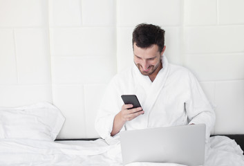 Fototapeta premium Happy handsome man using laptop in bed in the morning