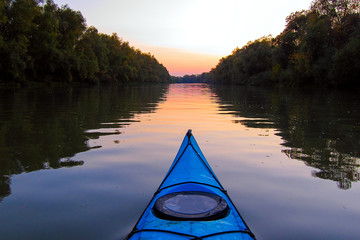 Bow of blue kayak on Danube river at dusk. Kayaking on calm autumn river in the evening. View on river from the bow of kayak - obrazy, fototapety, plakaty