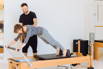 Hansdome beard man pilates instructor consulting female with cute two braids hairstyle workout on...