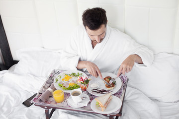 Obraz na płótnie Canvas Happy single man eating breakfast in bed