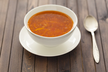 Chicken soup with vegetables and herbs in a white bowl on a wooden table