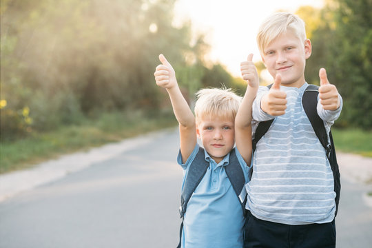 Two heerful blondy boys gives a thumbs-up. Schoolboys smiling and happy.