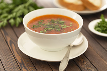 Chicken soup with vegetables and herbs in a white bowl on a wooden table