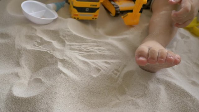 happy child playing toy in sand playground, close-up baby barefoot