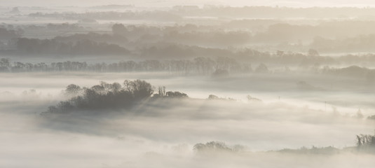 Stunning foggy English rural landscape at sunrise in Winter with layers rolling through the fields