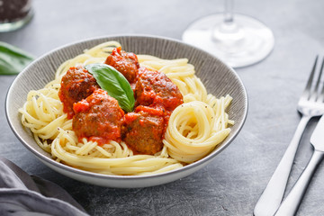 Beef meatballs in tomato sauce with Italian spaghetti and fresh basil leaf on a dinner table....