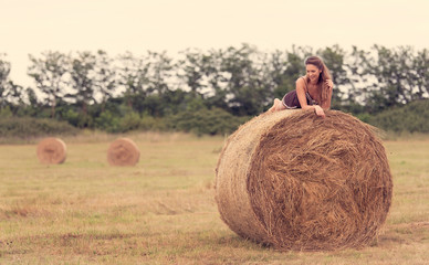 Naklejka na ściany i meble Beautiful woman relaxing on hay bale
