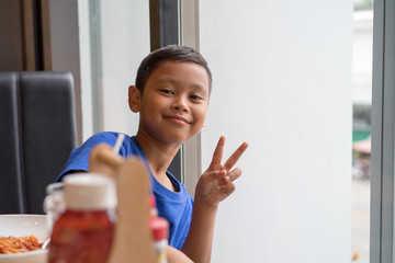 Cute asian boy seat at window eating food in a restaurant