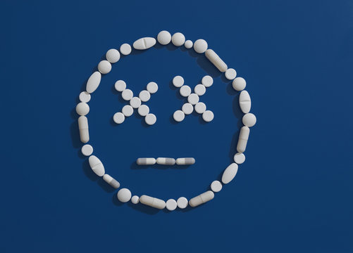 Pills forming dizzy face on blue background