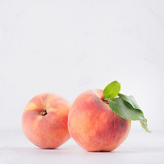 Two big ripe peaches with green leaves on white light wooden table, copy space, closeup, square.
