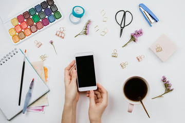 Flatlay of watercolors, brushes, sketchbook with blank page, cup of tea, smartphone with black...