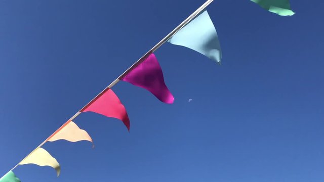Party flags in wind, clear blue sky background. Colorful festive flags against blue sky. Many colorful triangular flags blowing on wind on blue background. Pennant flying in wind with cute solid sky.