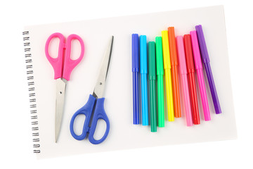 Set of colorful felt tip pens and two scissors on a blank, opened sketchbook sheet, isolated on white background. Art and creativity concept