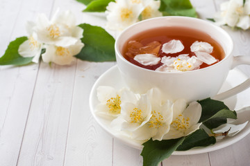 Mug of herbal tea with petals of Jasmine flowers on a light background.