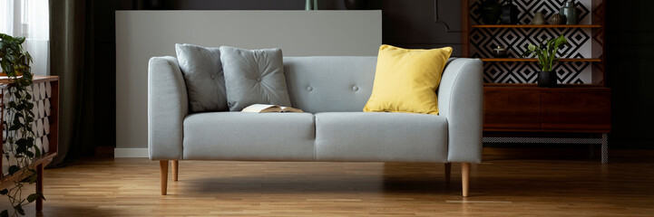 Grey sofa with yellow cushion and open book in real photo of dark vintage living room interior