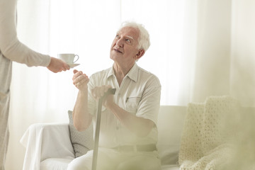 Grandfather holding a cane and getting a tea from his wife