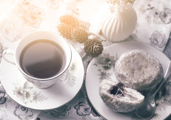 Soft focus of home made jam doughnuts with burry background of cup of hot blueberry tea in retro filter, Afternoon tea served with strawberry jam donut in sunny day autumn, English traditional