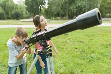 Children teenagers in the park looking through a telescope