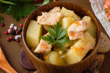Potatoes stewed with chicken and vegetables in a wooden bowl.