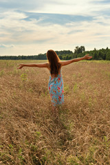 young woman girl standing with her back with open arms to the sunset on a wheat field in the...
