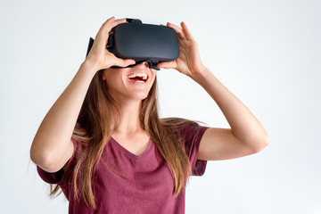 Smiling positive woman wearing virtual reality goggles headset, vr box. Connection, technology, new generation, progress concept. Girl trying to touch objects in virtual reality. Studio shot on gray