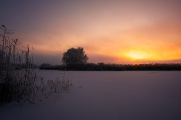 Beautiful winter landscape. Foggy morning sunrise. Colorful evening, bright sunshine over a river or lake.