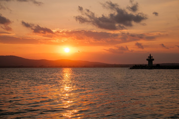 Lighthouse against a beautiful evening sunset on the sea. Amazing sunset on black sea and beautiful cloudscape.