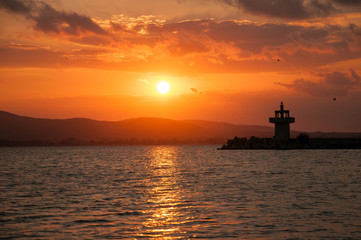 Lighthouse against a beautiful evening sunset on the sea. Amazing sunset on black sea and beautiful cloudscape.