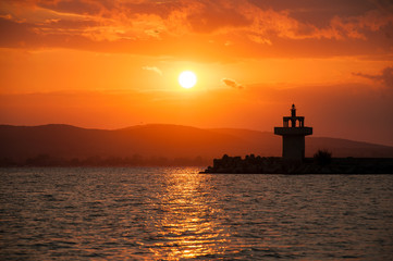 Lighthouse against a beautiful evening sunset on the sea. Amazing sunset on black sea and beautiful cloudscape.