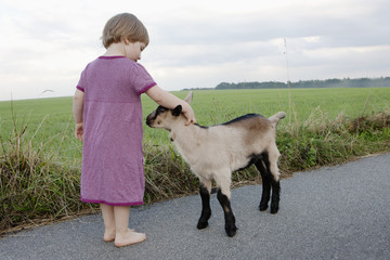 Cute girl petting goat on rural road