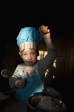 Portrait cute girl in chefs hat baking, holding egg