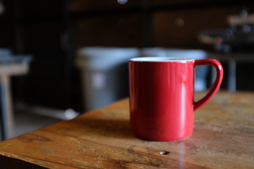 Close up side of a red cup of coffee on a rustic wooden table in a cafe with blurred background