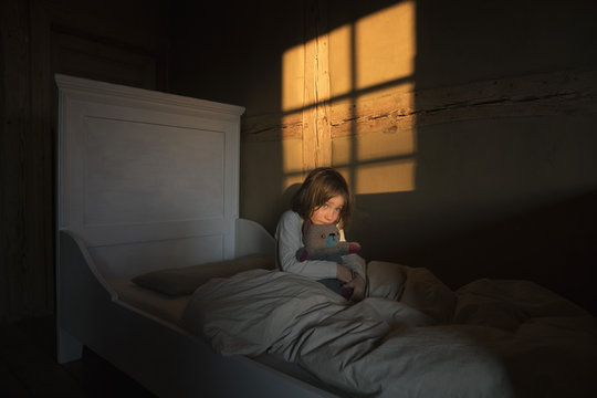 Afraid girl laying in bed with teddy bear