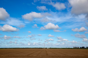 White fluffy clouds float above a ploughed field in a rural area