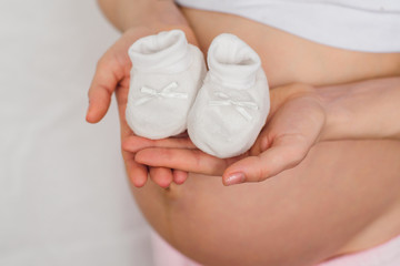 Fototapeta na wymiar booties for newborn in the hands of a pregnant girl on the background of the abdomen waiting for the baby