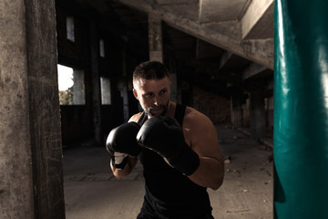 Fototapeta na wymiar Male boxer punching a boxing bag in warehouse.