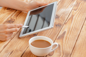 Close-up of young female hands holding digital tablet and drinking morning macchiato.