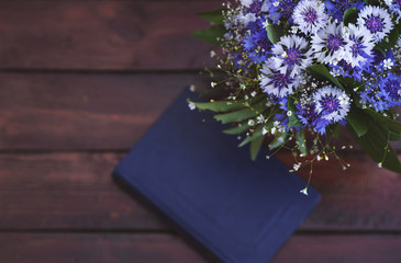A beautiful bouquet of cornflowers in vase and book on the wooden background with a copy space for text