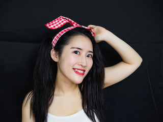 Portrait of good looking sexy Chinese woman with long black hair, pink hair ribbon and white halter against black background, looking and smiling at camera.