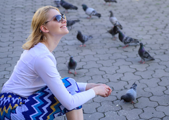 Girl blonde woman relaxing city square and feeding pigeons. Woman tourist or citizen toss crumbs...