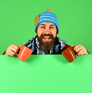 Man in warm hat holds brown cups on green background