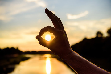 Silhouette ok hand gesture in front of sunset above river water surface. Sunset sunlight romantic...
