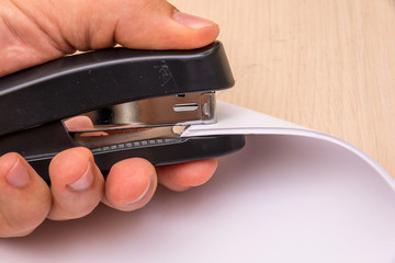 A black stapler in his hand pierces many sheets of paper